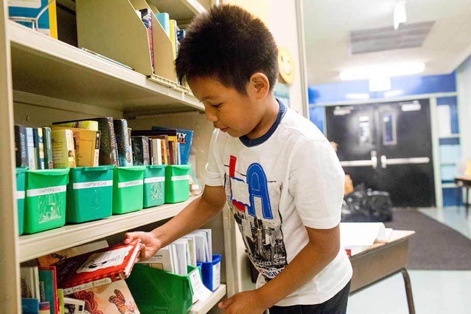 Child getting a book from green bins on a shelf